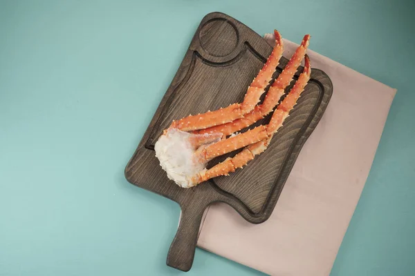 Fresh tasty king kamchatka crab\'s claw with lemon slices on wood board at brown and blue background