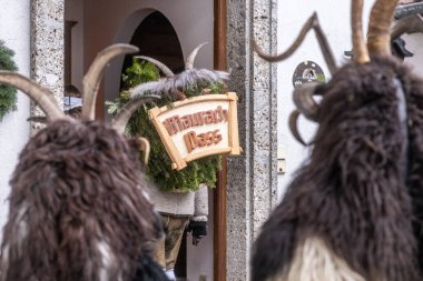 İnsanlar yerel bir geleneği kutlamak için köy meydanında toplanıyorlar. Kostümlü figürler bir işaret taşırken, diğerleri şenlikli atmosferin tadını çıkarıyor..