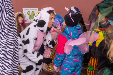 İnek kostümü giymiş biri renkli kıyafetler giymiş çocuklar için saksafon çalıyor.