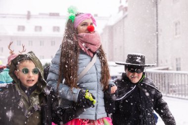 Renkli kostümlü üç çocuk kış şenliklerinde karda birlikte yürürler.