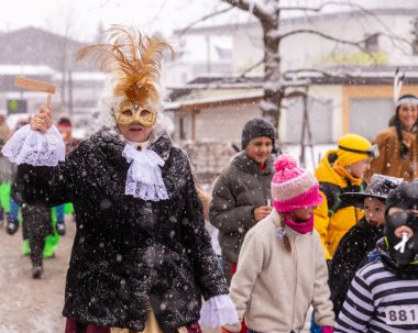 Karlı bir kış festivalinde, süslü kostüm giymiş bir kadın sanatçı çocuklarla birlikte yürüyor.