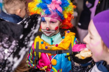 Renkli peruğu ve renkli yüzü olan palyaço kostümlü bir çocuk.