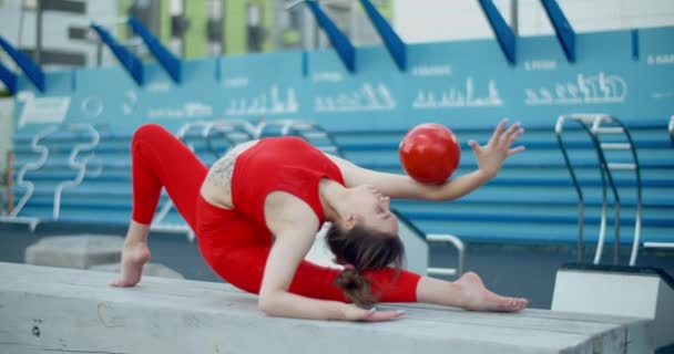 Woman in red sports costume performing callisthenics exercises with gymnastic ball at workout playground outdoors, sports in the urban environment, gymnastics in the city, 4k 120p Prores HQ — Stock Video