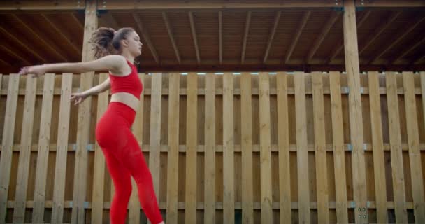 Молодая гимнастка в красных прыжках в замедленной съемке, женщина выполняет большой джет на открытом воздухе, акробатика в городе, тренировки на открытом воздухе, callisthenics в замедленной съемке, 4k 120p Прорес HQ 10 бит — стоковое видео