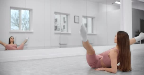 Tancerka siedzi na sznurku i rozgrzewa się przed ścianą lustra w białej jasnej sali tanecznej, próba baletu, balerina w studiu baletowym, lekcja tańca, kwatera główna 4k 60p Prores — Wideo stockowe
