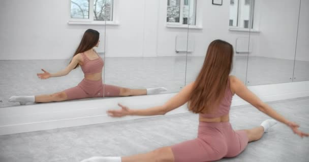 Dancer sitter på garnet och värmer upp framför spegelväggen i den vita ljusa danssalen, balett repetition, ballerina i balett studio, danssal lektion, 4k 60p Prores HQ — Stockvideo