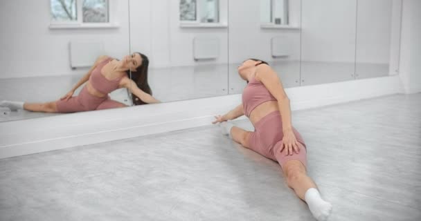 La ballerina è seduta sullo spago e fa curve davanti alla parete dello specchio nella luminosa sala da ballo bianca, prove di danza classica, ballerina nello studio di danza, lezione di sala da ballo, quartier generale di 4k 60p Prores — Video Stock