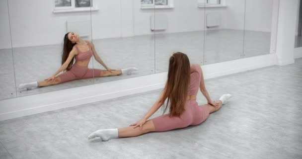 Dancer zit op het touw en warmt zich op aan de voorzijde van de spiegelwand in de witte heldere danszaal, balletrepetitie, ballerina in de balletstudio, dansles, 4k 60p Prores HQ — Stockvideo