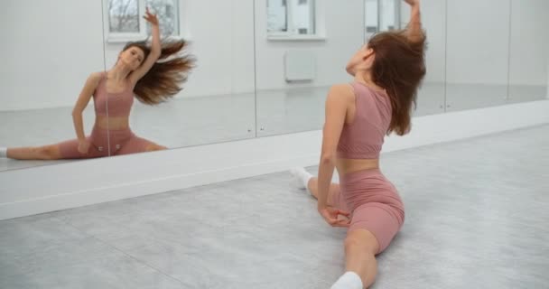 Tanečnice sedí na provázku a zahřívá se před zrcadlovou stěnou v bílém jasném tanečním sále, baletní zkouška, baletka v baletním studiu, lekce tanečního sálu, štáb 4k 60p Prores — Stock video
