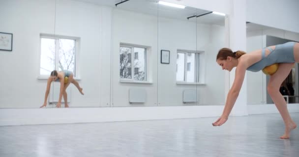 Žena sportovec provádí kallisthenics cvičení s gymnastický míč na podlaze v bílém tanečním sále, sportovní cvičení před zrcadlovou stěnou, gymnastika v bílé hale, 4k 120p Prores HQ — Stock video