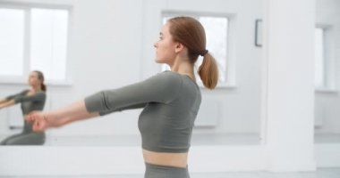 Sıkı vücut kıvrımlı jimnastik yapan kadın pilates ve esneme egzersizlerini beyaz yoga salonunun zemininde, yoga egzersizleri, yoga ve pilates eğitimi, 4k 120p Prores karargahında yapıyor.