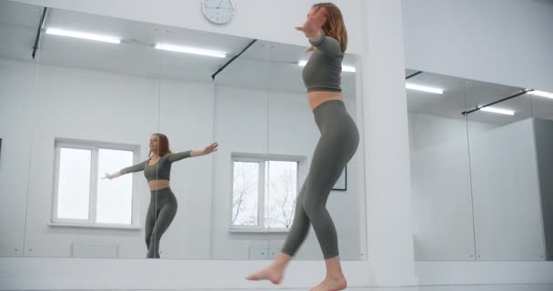 Turnerin springt in Zeitlupe vor Spiegelwand in der weißen Halle, Turnen in der weißen Halle, Yoga- und Pilatetrainer, 4k 120p Prores HQ — Stockvideo