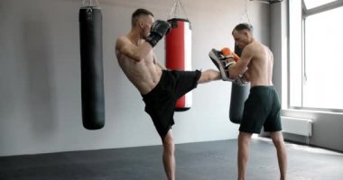 Kickboksör orta vuruşunu spor salonunda ağır çekimde antrenörle yapıyor, karma dövüş sanatları dövüşçüsü antrenman yapıyor, 4k 120fps Prores HQ