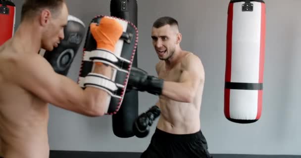 Bojovník v boxerských rukavicích cvičí své údery s trenérem ve zpomaleném filmu v tělocvičně, kickboxeři trénují, 4k 120fps Prores HQ — Stock video