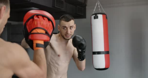 Myśliwiec w rękawicach bokserskich ćwiczy uderzenia z trenerem w zwolnionym tempie na siłowni, kickboxerzy trenują, 4k 120fps Prores HQ — Wideo stockowe