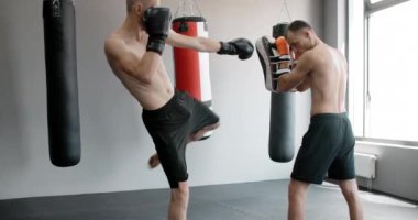 Kickboksör orta vuruşunu spor salonunda ağır çekimde antrenörle yapıyor, karma dövüş sanatları dövüşçüsü antrenman yapıyor, 4k 120fps Prores HQ