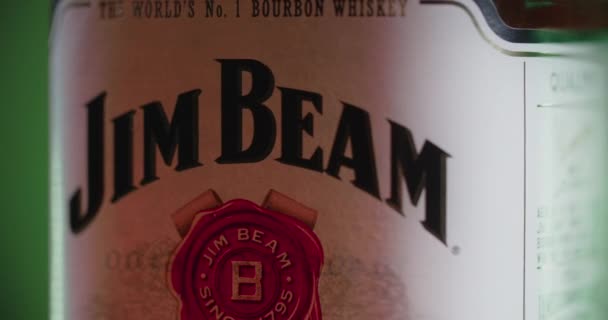 WAARSCHUWING, POLEN - SEPTEMBER 10, 2021: close-up van de fles Jim Beam bourbon die ronddraait op de groene achtergrond, 4k 60p Prores HQ — Stockvideo