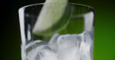 Viski bardağına yeşil arka planda kokteyl ve buz küpleriyle birlikte limon dilimi eklendi. 4k 60 peni Prores HQ.