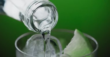 Soda dar boğazdan soğuk içecekle bardağa, limonata, buz küpleri ve soda ile doldurulur. Yeşil arkaplandaki mohito kokteylinin yapımı, 4k 60p Prores HQ