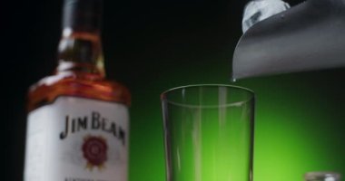 POLAND - 10 EYLÜL 2021: Buz küpü, arka planda Jim Beam viskisi şişesi ile ağır çekimde Highball 'a bırakılıyor, 4k 120p Prores HQ