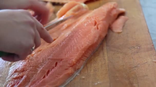 Kocken skär upp laxrosa fisk med kniv i trä styrelsen på bordet — Stockvideo