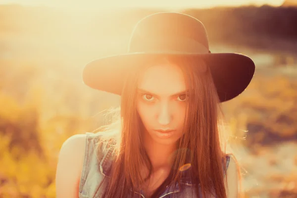 Дівчина в чорному капелюсі позує на заході сонця — стокове фото