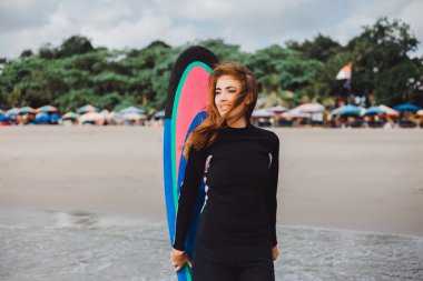 girl in wetsuit with surfboard