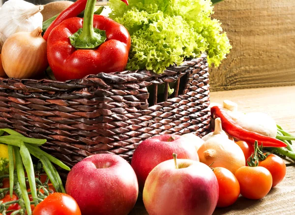 Cesta de vime com frutas e legumes em mesa de madeira — Fotografia de Stock