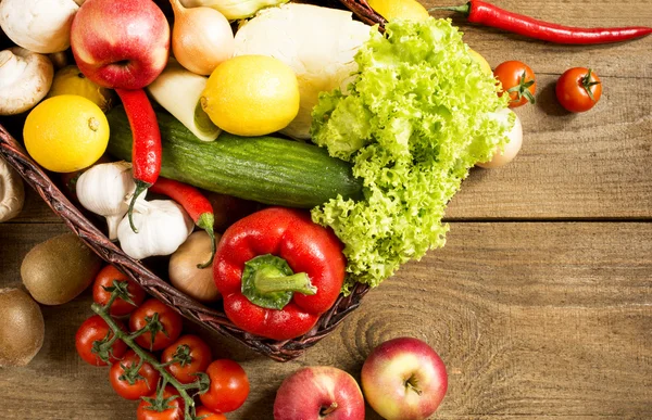 Cesta de vime com frutas e legumes em mesa de madeira — Fotografia de Stock