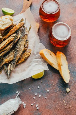 Kızarmış balık ançüezi, bardakta bira, ekmek, limon ve beton arka planda tuz.