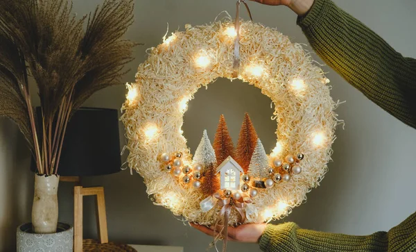 Corona de Navidad hecha a mano con luces en las manos de la mujer para las vacaciones de invierno tradición, guirnalda ligera, materiales naturales y ecológicos —  Fotos de Stock