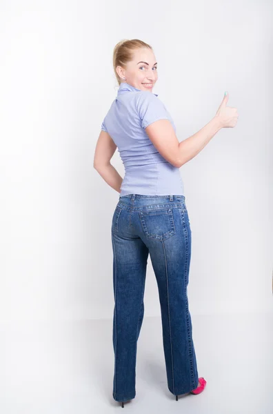Красива молода ніжна блондинка в джинсах і синя сорочка в чоботях, позує на повну висоту, показує великий палець — стокове фото