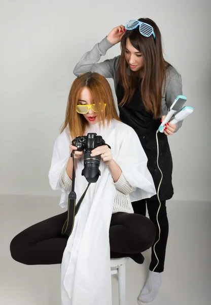 Beautiful young leggy redhaired model looks pictures on the camera, hairdresser does a hairstyle. two girls with glasses disco — Stock fotografie