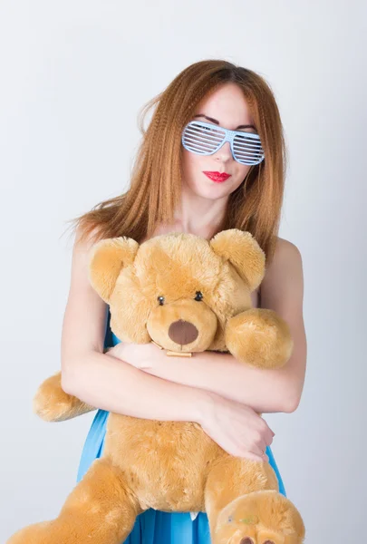 Chica en un vestido azul y gafas de sol en el estilo de discoteca, abrazando a un oso de peluche en los mismos vasos — Foto de Stock