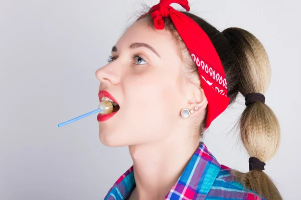 Close-up bela jovem menina loira de pernas em uma bandana vermelha, macacão jeans e uma camisa xadrez, lambendo doces — Fotografia de Stock