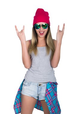 denim şort ve gri bir t-shirt ve pembe bir örgü şapka genç kız, kalça ekose gömlek bağlı. işaret ağır metal kadar başparmak gösteren. beyaz arka plan üzerinde izole