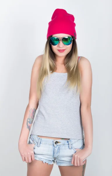 Adolescente en pantalones cortos de mezclilla y una camiseta gris y un sombrero de punto rosa, atado a la camisa a cuadros de las caderas. chica en gafas de sol — Foto de Stock