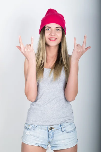 Teenager girl in denim shorts and a gray T-shirt and a pink knit hat, tied at the hips plaid shirt. showing sign heavy metal — Stock Photo, Image