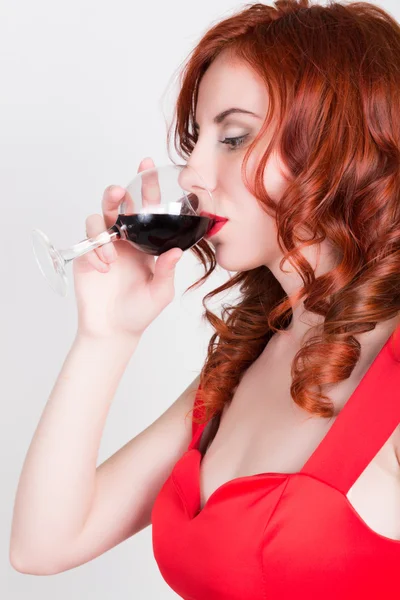 Close-up portrait of Elegant young redhead woman in a red dress, having a glass of red wine — Stockfoto