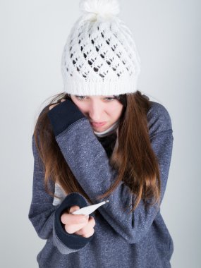 young woman in a knitted hat and scarf, holding hands in the thermometer. she seems sick clipart