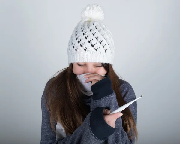 Молода жінка в в'язаному капелюсі і шарфі, тримаючись за руки в термометрі. вона здається хвора — стокове фото