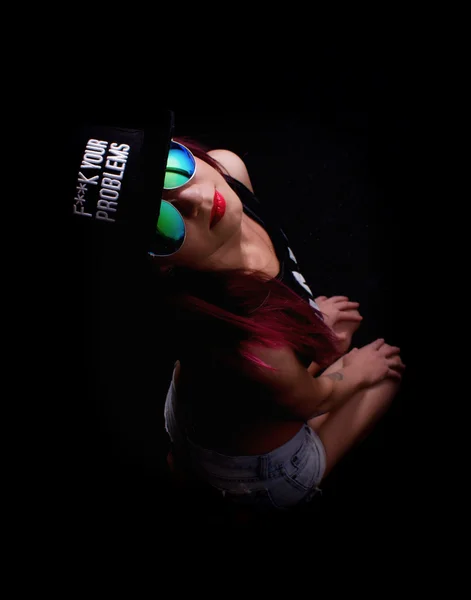 Attractive young woman in cap and sunglasses, smokes on a dark background. Be trendy, be rapper — Stock Photo, Image