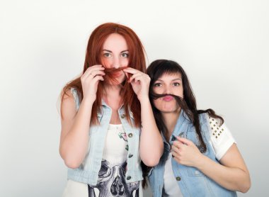 İki genç kız arkadaş şımartMak ve grimace, saçlarından bir bıyık birbirlerini yapmak. Saçtan bıyık yapan genç