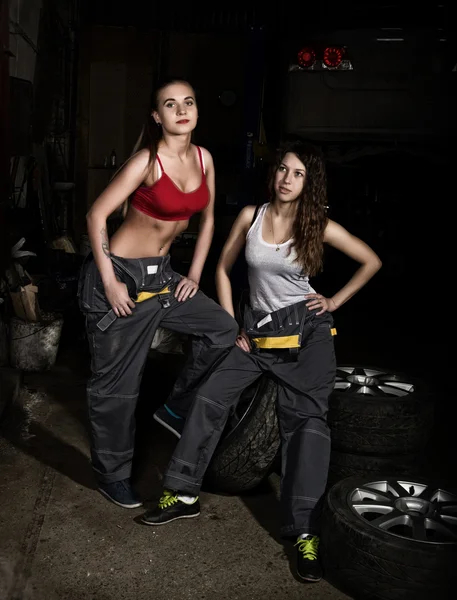 Sexy meninas mecânico sentado em um pneu segurando uma chave na mão em um carro reparos. conceito de vida incolor — Fotografia de Stock