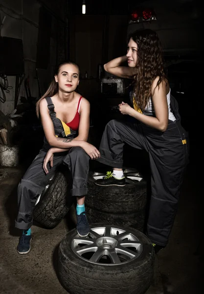 Sexy Mädchen Mechaniker sitzt auf einem Reifen mit einem Schraubenschlüssel in der Hand auf einem Auto Reparatur. Farbloses Lebenskonzept — Stockfoto