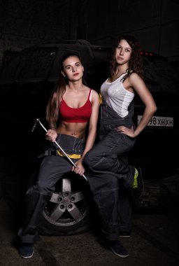 sexy girls mechanic sitting on a tire holding a wrench in his hand on a car repairs. colorless life concept