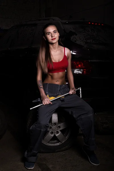 Sexy girl mechanic sitting on a tire holding a wrench in his hand. colorless life concept — Stock Photo, Image