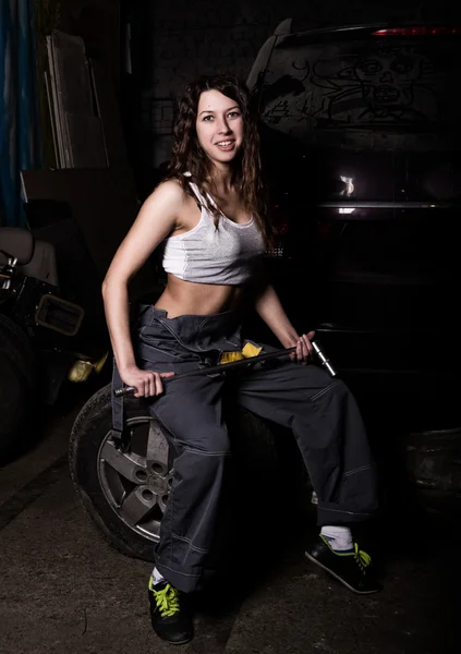 Sexy chica mecánica sentado en un neumático sosteniendo una llave inglesa en su mano. concepto de vida incoloro — Foto de Stock