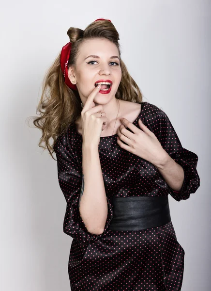 Sexy young blond with long curly hair in a black polka-dot dress, put her index finger to her red lips — Stock Photo, Image