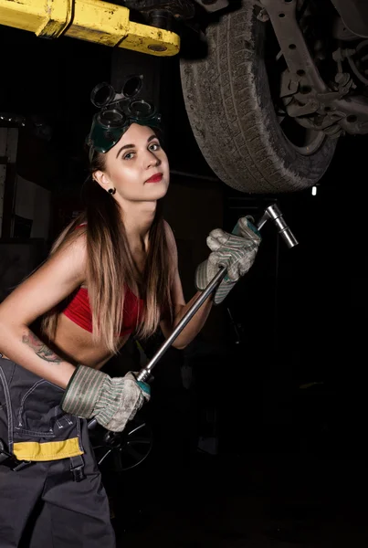 Krásná mladá samička, která prověřujte auto v autoopravně. mechanik v předevce mění kolo v garáži. Sexy mechanik — Stock fotografie